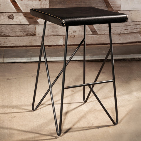 Saddle up to utility and beauty with Trestle stool, perfect behind your reception desk or at your make up counter. It's fabricated in a black iron rod frame, waxed finish. Topped with an upholstered seat cushion sewn with a large saddle stitch.